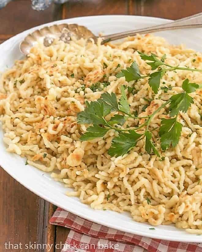 Spaetzle are German egg noodles that are the perfect alternative side dish to potatoes or rice. Learning how to make spatzle is fun with this easy spatzle recipe! Spaetzel topped with parsley sprig on a white platter.