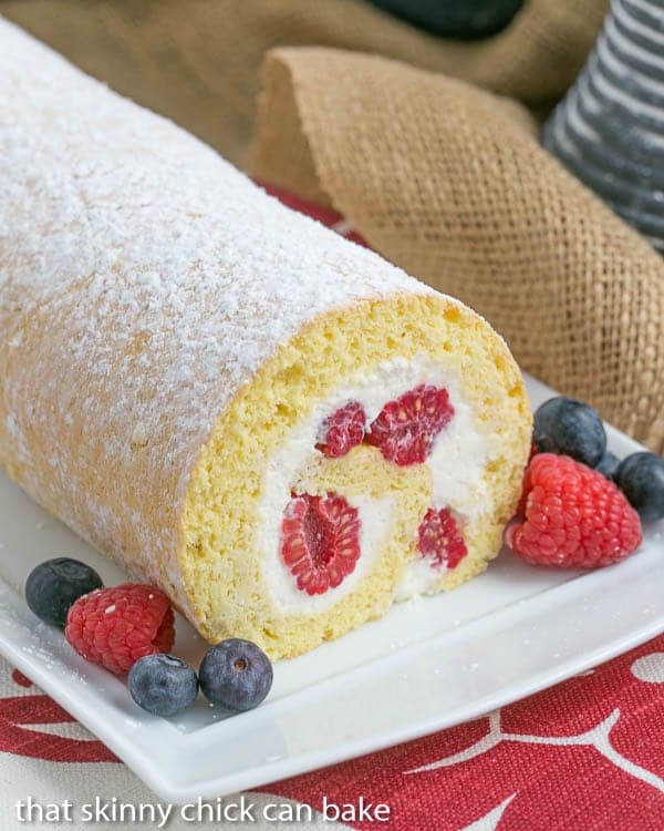 Berry Mascarpone Roulade - a sponge cake rolled around berries and a scrumptious mascarpone cream filling! Berry Roulade on a white serving tray with a garnish of fresh berries.
