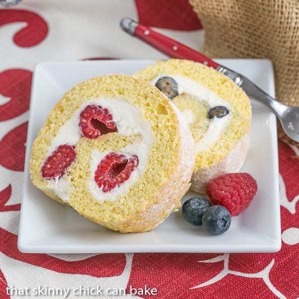 Berry Mascarpone Roulade - a sponge cake rolled around berries and a scrumptious mascarpone cream filling! Slices of Berry Roulade on a square white plate with fresh berries to garnish.