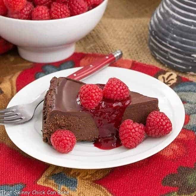 Flourless Chocolate Torte with Raspberry Sauce - A decadent gluten free flourless chocolate torte topped with chocolate ganache #chocolate #desserts #valentinesday A slice of Chocolate Torte on a white dessert plate.
