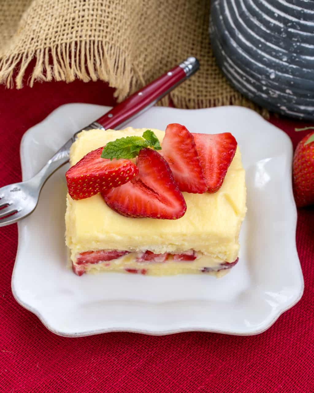 Berry Tiramisu with Grand Marnier - A strawberry twist on the Italian classic with mascarpone and Grand Marnier soaked ladyfingers! Berry Tiramisu with Grand Marnier slice on a square white plate with a red handled fork.