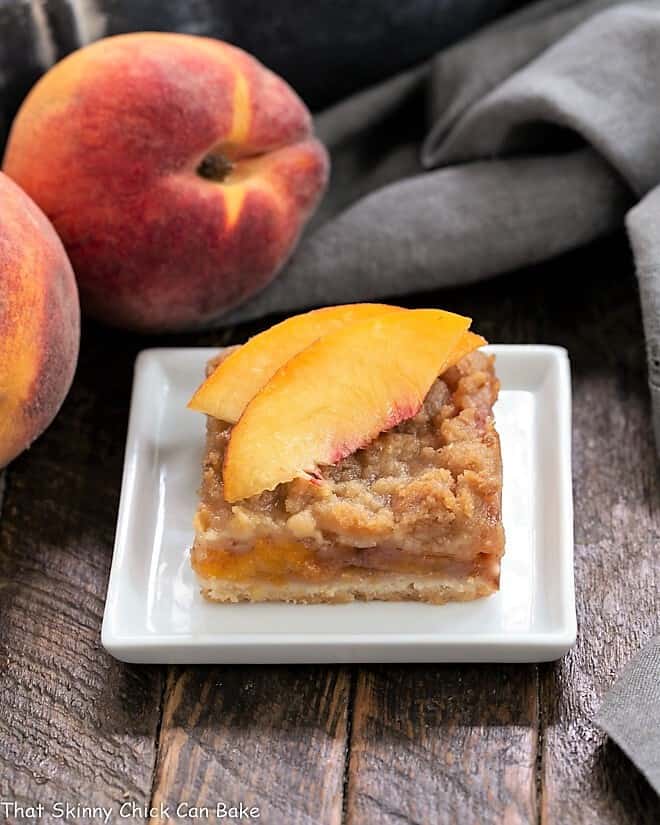 Fresh Peach Pie Bars - A shortbread crust topped with sweetened peaches and a streusel topping! Fresh Peach Pie Bar on a white plate topped with peach slices