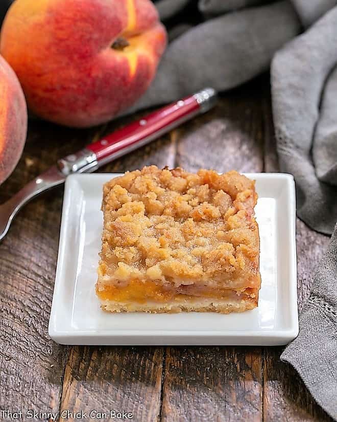 Fresh Peach Pie Bars - A shortbread crust topped with sweetened peaches and a streusel topping! A fresh peach bar on a square white plate