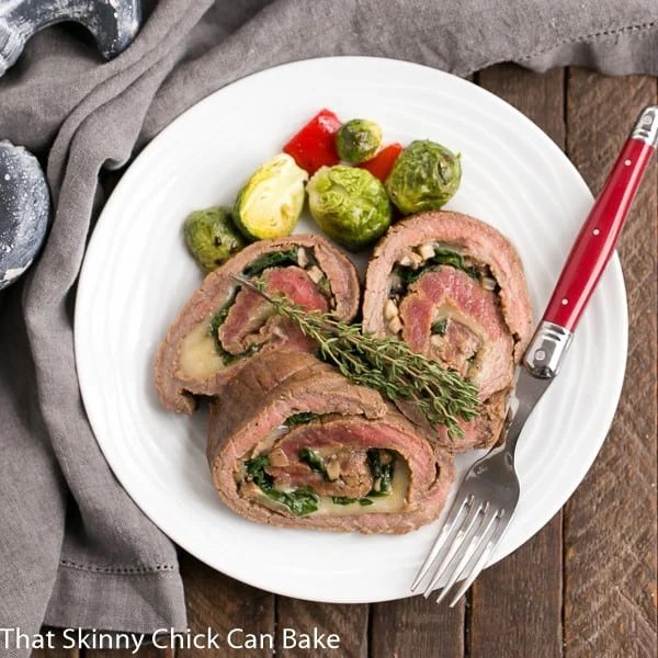 Flank Steak Roulades - A butterflied steak filled with spinach, mushrooms and Provolone cheese Overhead view of Flank Steak Roulades on a white dinner plate.
