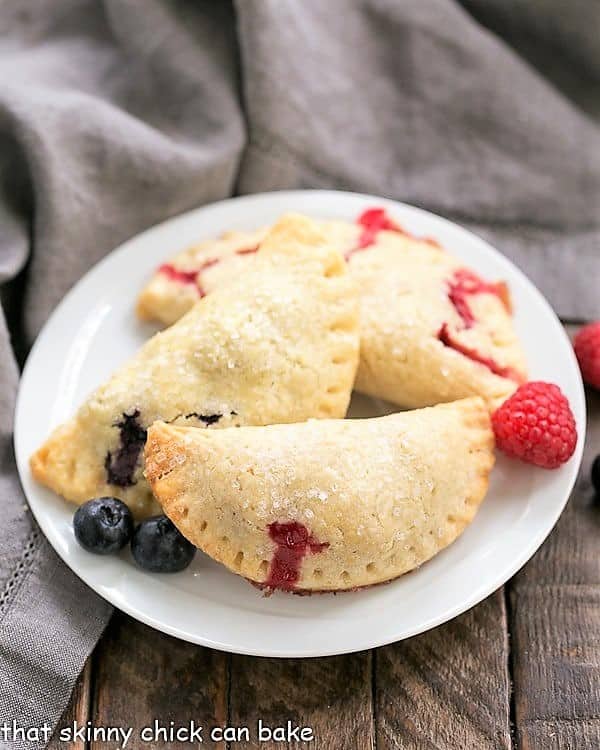 Rustic Berry Turnovers - Buttery crusts + sweetened berries make these fabulous hand pies! Rustic Berry Turnovers on a round white plate.