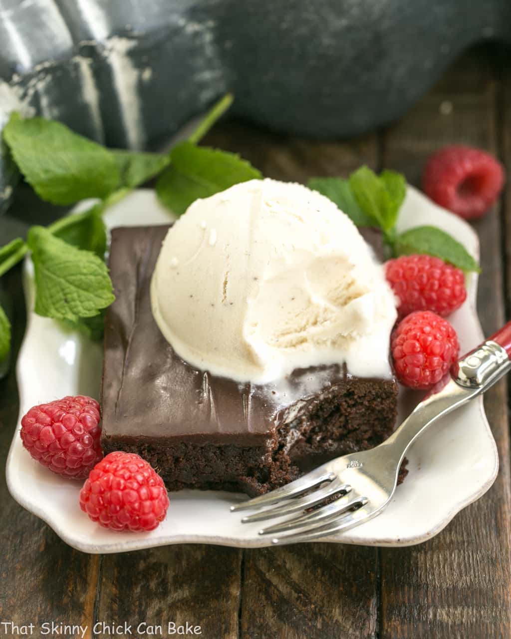 Fudgy Chocolate Sheet Cake with Cocoa Icing - A delectable, ultra-chocolate dessert that feeds a crowd! #sheetcake #chocolate Fudgy Chocolate Sheet Cake with Cocoa Icing on a white dessert plate with ice cream, mint and raspberries.