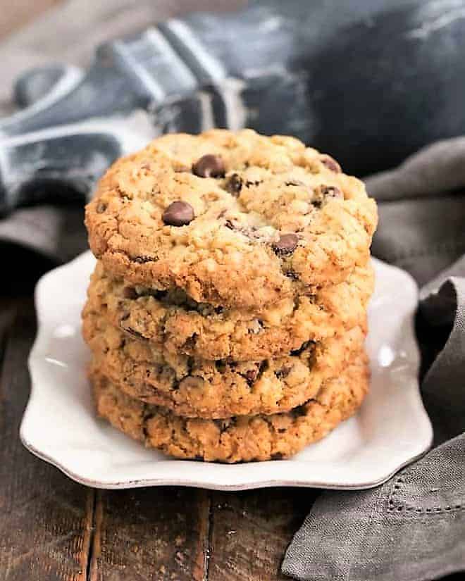 Cowboy Cookies Recipe - Chewy, buttery cookies with oats, chocolate chips, pecans and coconut 4 cowboy cookies stacked on a square white plate.