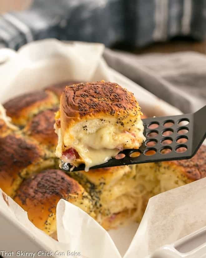 Corned Beef Sliders - All the fabulous flavors of a Reuben Sandwich in a slider! Corned Beef Sliders in a white casserole dish with a single slider on a black spatula.