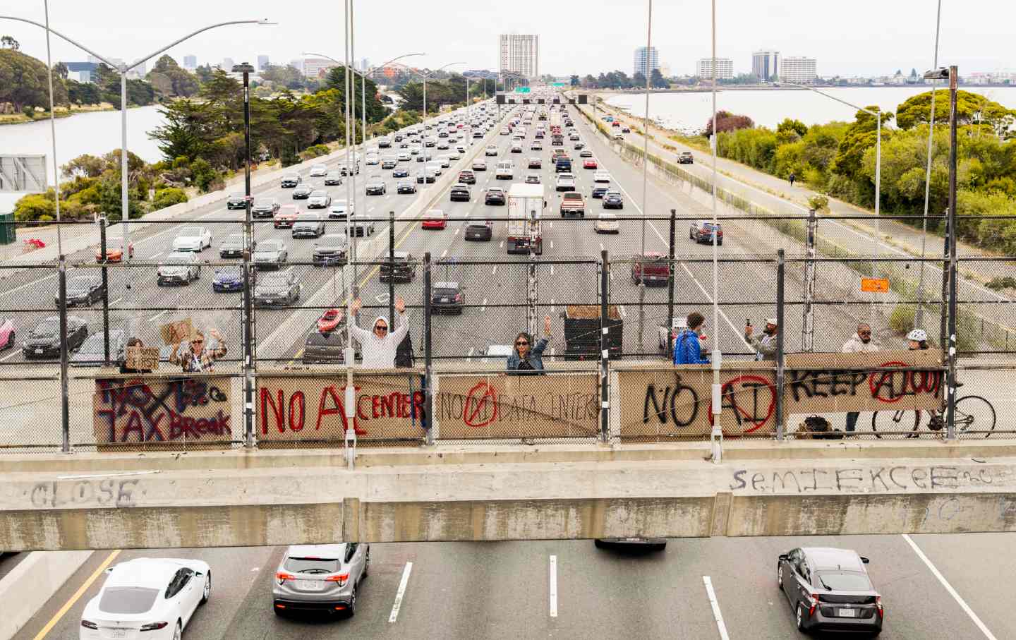 People hold up signs on a pedestrian bridge during a nationwide protest against AI data center expansion in Berkeley, California, on July 18, 2026.