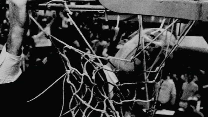 DaleBrownBitingNet | TigerRag.com Close-up of a worn basketball net with players and spectators visible in the background.