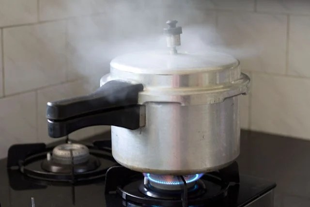 sarson-ka-saag7 pressure cooker on a stove with steam coming out.