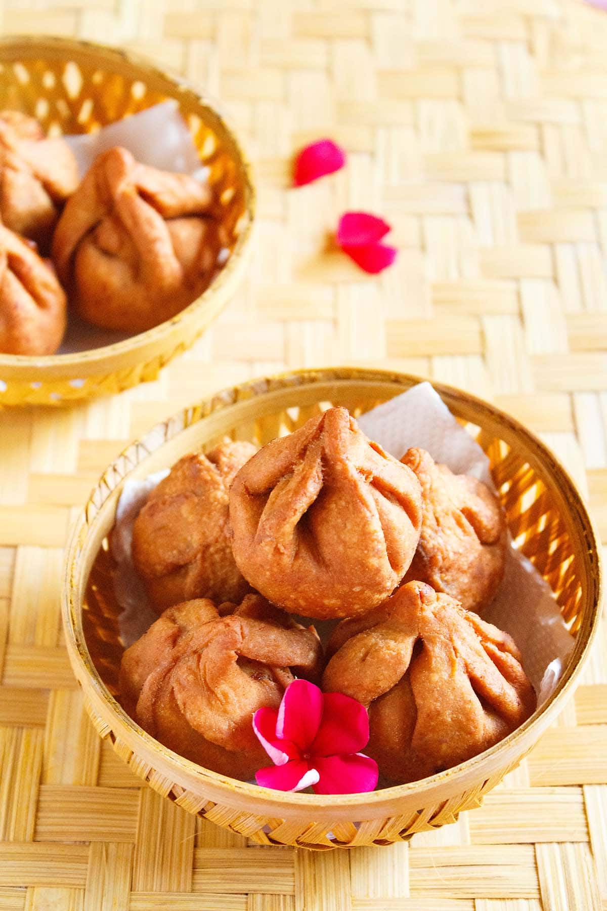 fried modak fried modak in a round bamboo bowl with a dark pink flower placed on a bamboo mat