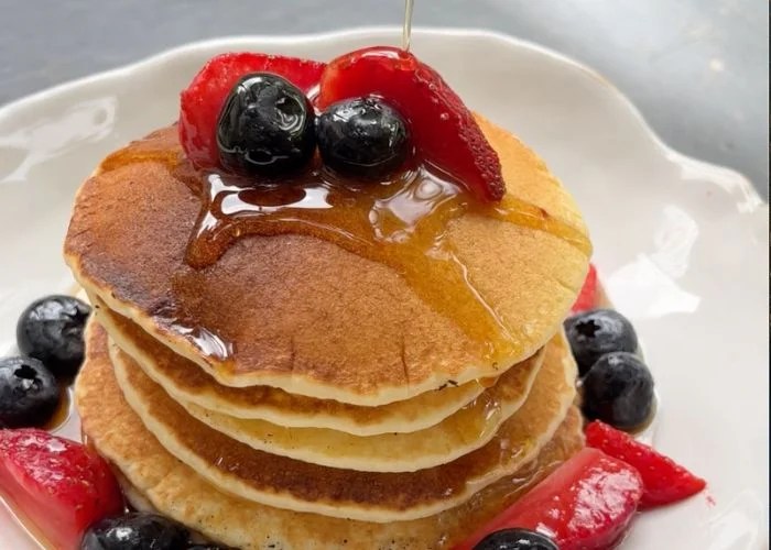 stack of pancakes served with berries drizzled with maple syrup on a white plate