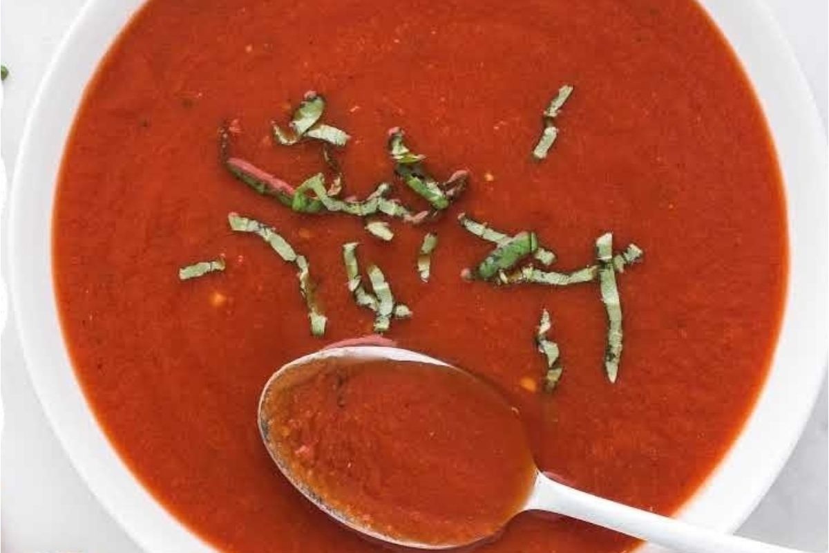 Tomato soup recipe served in a white bowl with a spoon.