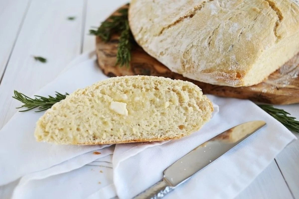 A loaf of bread with rosemary sprigs on a wooden board, perfect for trying different bread recipes.