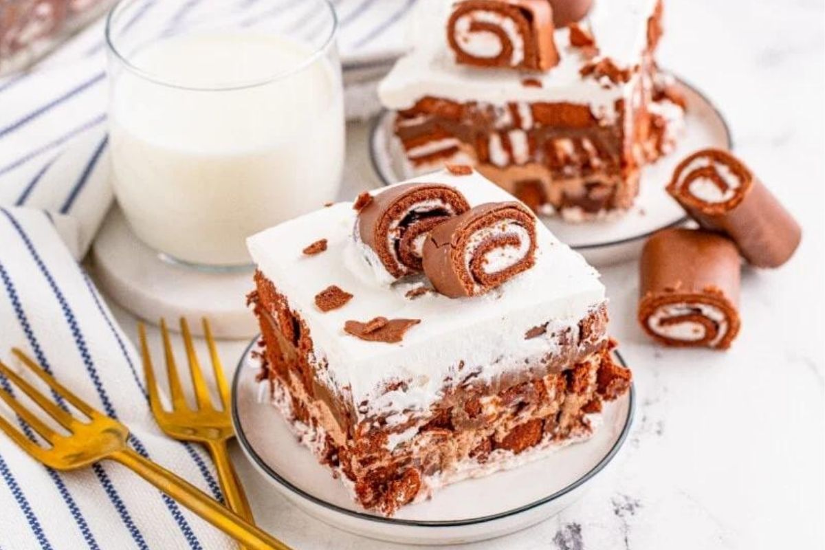 A slice of creamy chocolate roll cake served with a glass of milk.
