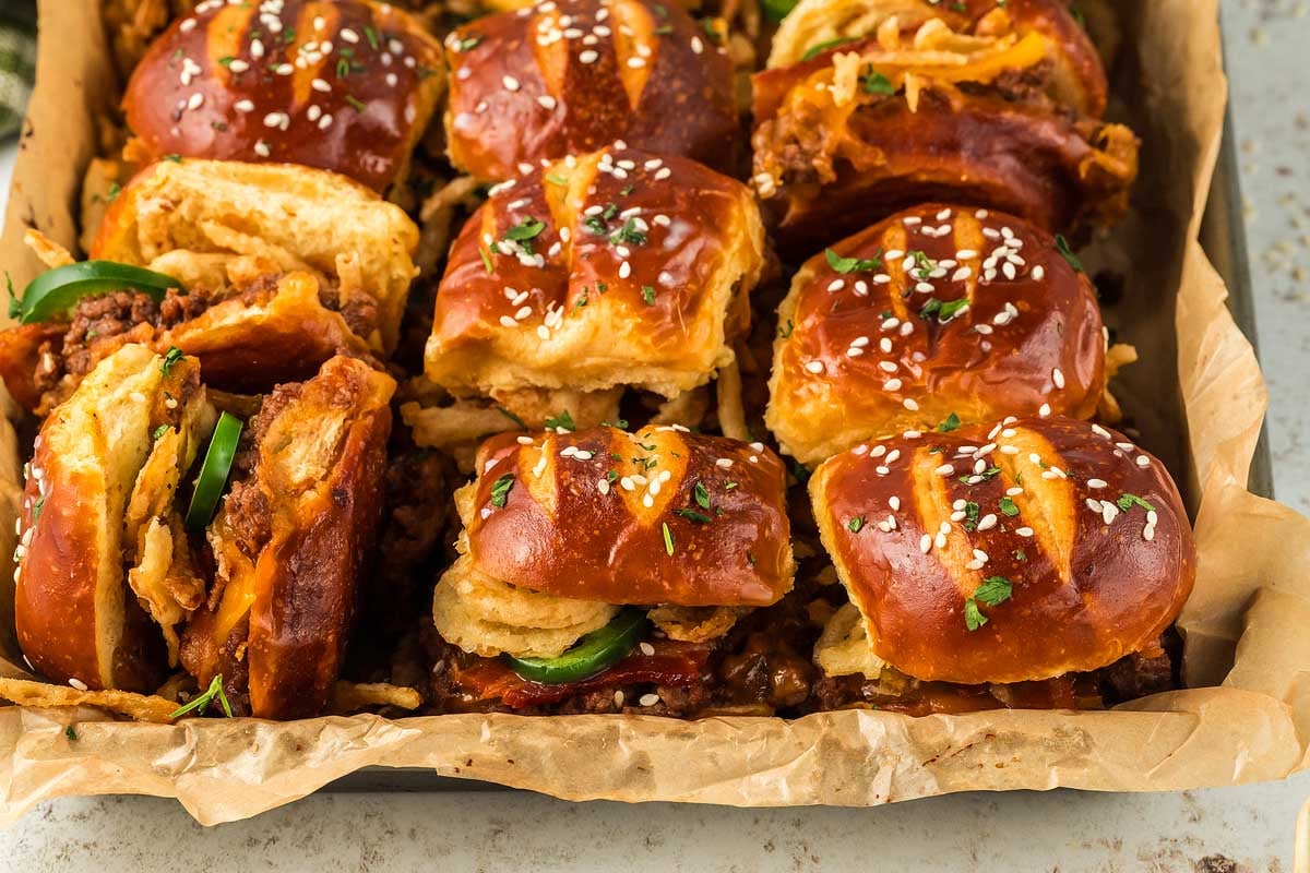 A tray of cowboy sliders with pretzel buns, crispy chicken, caramelized onions, and a sprinkle of sesame seeds.